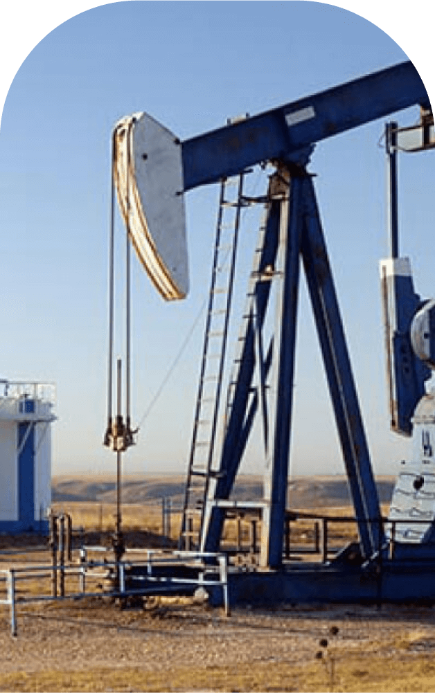 Close-up view of a pumpjack operating at a crude oil extraction site, illustrating the type of equipment used in crude oil pumping processes, with storage tanks visible in the background under a clear sky.